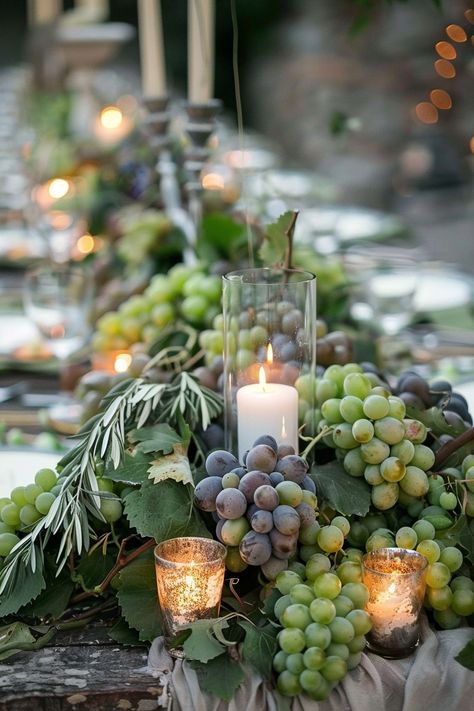 ✨ Elevate your wedding ambiance with a centerpiece that whisks you away to the rolling hills of Tuscany. Experience the charm of Italy as grape vines & olive branches intertwine with the warm glow of candles on your special day. #WeddingInspiration #TuscanWedding #RomanticDecor #WeddingIdeas #CountryChic #RusticElegance #GrapeAndOlive #CandlelightMagic Let the light guide your love story. Grape Vines Decor Ideas, Olive Leaf Centerpiece Wedding, Grapevine Wedding Decor, Grapes On Wedding Table, Wedding Table Olive Branch, Olive Theme Wedding Table Settings, Vineyard Table Decor, Grape Centerpiece Wedding, Olive Branches Decor