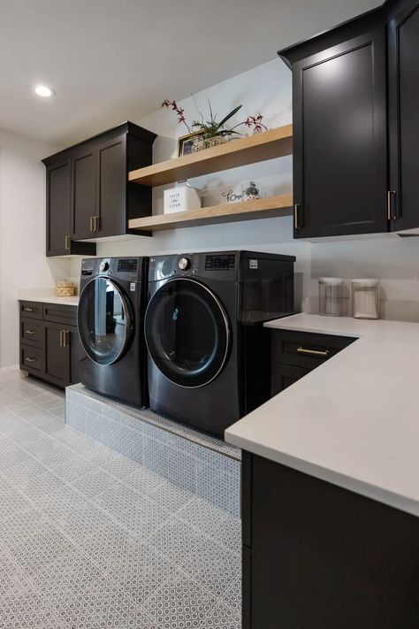 This modern laundry room exudes style with bold black appliances elevated on a step, sleek black cabinetry, and open shelving for a functional yet elegant design. The striking patterned tile adds a touch of personality to the space, elevating the overall aesthetic. With a perfect balance of style and practicality, this laundry room transforms the everyday chore into a chic experience. Ideal for those looking to add sophistication and organization to their home’s functional spaces. Laundry Room With Dark Appliances, Laundry Room With Black Cabinets, Laundry Room With Black Washer And Dryer, Black Washer And Dryer Laundry Room, Mid Century Modern Laundry Room, Laundry Room Aesthetic, Black And White Laundry Room, Black Laundry Room, Room Ideas Dark