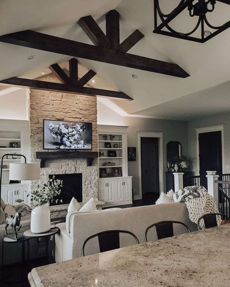 Black stained wood ceiling trusses in living room are mounted over a beige couch. The couch sits opposite a white to tan gradient painted stone fireplace with black wood mantel. Dark Ceiling Beams, Black Ceiling Beams, Wood Beam Ceiling Living Room, Beams In Living Room, Stained Wood Ceiling, Ceiling Trusses, Ceiling Beams Living Room, Stained Wood Beams, Painted Stone Fireplace