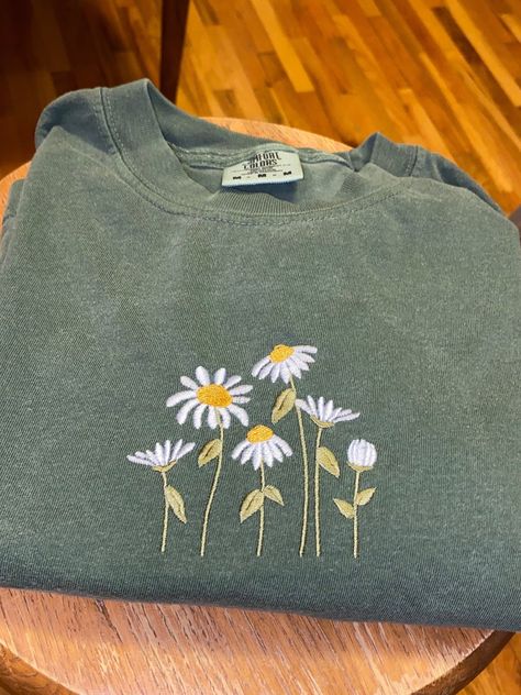 Vibrant daisies embroidered on a moss green T-shirt !! :)   The T-shirts I use are comfort colors brand in adult unisex sizing! Hand Embroidery T Shirt Ideas, Green Shirt Embroidery, Hand Embroidered Shirts For Women, Painting Shirt Ideas, Embroidery On T Shirt, Embroidered Clothes Ideas, Embroider Daisies, Embroidery Shirt Ideas, Embroidery Ideas Clothes