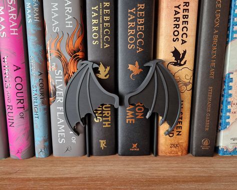 Add a touch of fantasy to your bookshelf with our Peekout Sign featuring dragon wings. Perfect for book lovers and fantasy enthusiasts! You can choose between a set of two dragon wings (one left and one right) or a single wing. The sign consists of two easy-to-assemble pieces (the Dragon Wing and a backsheet) that slide between your books. The backsheet can be used for all of our peekout signs, so you can easily switch between colors or words! Sizes: ♥ 1 Dragon Wing: 8 x 11 cm ♥ Backsheet: 7.7 x 14 cm Materials: Every sign is produced using our own 3D printers, right in our workspace! They are made of PLA. Due to the nature of 3D printing, there may be slight imperfections, making each piece uniquely yours. Dragon Room Aesthetic, Game Of Thrones Book Nook, Library Book Nook, Bookish Home, Forest Book Nook Shelf Insert, Harry Potter Dragon Folded Book Sculpture, Dragon Bookends, Bedroom Furniture Inspiration, Bookshelf Decoration