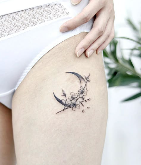 Moon Tattoos: Upper Thigh Crescent Moon With Cherry Blossoms. A flower and moon tattoo with delicate lines and shading to make the cherry blossom petals pop. Click through for 53 moon tattoo ideas. #moontattoo #tattoos #tattooideas #flowertattoo IG: @aeri_tattoo Crescent Moon Tattoo Flowers, Carnation Moon Tattoo, Moon And Cherry Blossom Tattoo, Ribcage Moon Tattoo, Sakura Moon Tattoo, Sun Moon Star Flower Tattoo, Thigh Moon Tattoo, Sun Moon And Flower Tattoo, Moon And Vine Tattoo