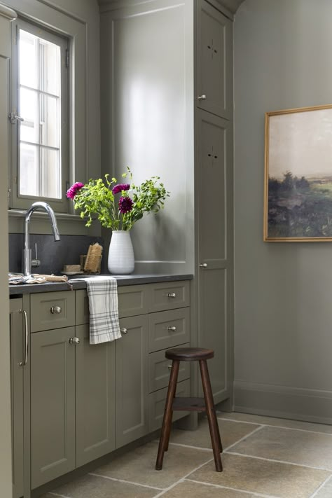 Green mudroom cabinetry with limestone flooring, polished nickel hardware, and dark countertops. Sw Cornwall Slate Cabinets, Sage Kitchen Cabinets Black Hardware, Green Kitchen Cabinets With Brushed Nickel Hardware, Green Cabinets Silver Hardware, Bathroom Green Countertop, Comfort Gray Kitchen Cabinets, Gray Kitchen Floor Tile, Dark Green Mudroom, Grey Green Kitchen Cabinets