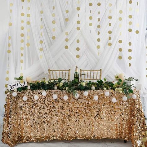 Ooze festive radiance by covering your couple’s table with a gold sequin tablecloth for the perfect glitz and glam. In order to exude refreshing vibes, arrange lovely rose garlands on the front edge of the table and illume your display using a variety of candles and ball string lights. Add a pop of greenery by arranging fake succulents in white wooden boxes. Whereas, create a serene backdrop using white curtains and adorn them with circle-shaped paper garlands for a glamorous look. Paper Circle Garland, Sweetheart Table Backdrop, Hanging Backdrop, Elegant Table Decorations, Gold Glitter Paper, Streamer Backdrop, Paper Circle, Circle Garland, Party Girlande