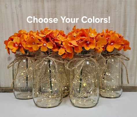 "This six piece set includes your choice of hydrangea color. Choose pint size or quart size...or a set of both. Each centerpiece jar includes one set of warm white LED fairy lights, and one silk hydrangea, and a jute bow.  These centerpieces are very popular for weddings, baby showers, parties, corporate events, holiday events, and any other event that requires table centerpieces. They also look great in any room of your house or office. To see other lighted jar options and all of my other listings, please view my shop: https://www.etsy.com/shop/GlassyGalDecor  Listing pic: Orange hydrangeas in quart size jars are shown in this listing pic, but other color choices are available. Each jar set includes: (1) clear mason jar (1) set of LED fairy lights (1) faux hydrangea stem (1) jute bow Dime Wedding Centerpieces With Lights, Lighted Mason Jar Centerpieces, Orange Hydrangeas, Mason Jars With Lights, Christmas Arrangements Centerpieces, Event Centerpieces, Lighted Centerpieces, Farmhouse Centerpiece, Hydrangea Colors