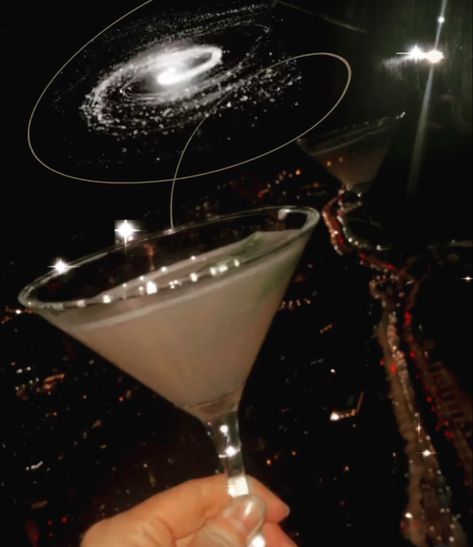 Sparkly martini pictured in front of a window showing a beautiful city skyline at night with shimmering city lights, Milky Way galaxy floats above martini Celestial Masquerade, Glittery Cocktail, Glitter Cocktails, City Skyscrapers, Light Cocktails, Martinis Drinks, Cocktail Martini, Art Window, Cake Aesthetic