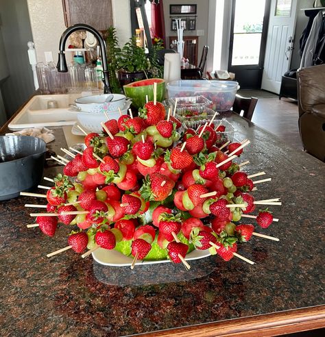 Cut a watermelon in half and scoop the middle into balls using a small scoop. Place the hollow part on a serving plate. Using wooden skewers, place a watermelon, green grape, red grape, and a strawberry to make the kebabs. Poke the ends into the watermelon rind to make the centerpiece. This is a pretty and easy way to serve fruit kebabs! Watermelon Fruit Basket Party Ideas, Strawberry Kebabs Skewers, Fruit In Watermelon Bowl, Fruit Shish Kebabs Skewers, Watermelon Basket Ideas, Watermelon Display Ideas, Fruit Screwers, Fruit Kebabs Ideas Skewers, Watermelon Display