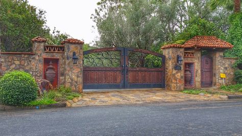 Spanish inspired driveway gate and pedestrian door beautifully constructed in Rancho Santa Fe, CA. Gated Home Exterior, Mexican Gates Hacienda Style, Spanish Driveway Gate, Spanish Fences And Gates, Hacienda Entrance Gates, Gated Entrance Landscaping, Spanish Style Driveway Gate, Mediterranean Gate Entrance, Hacienda Driveway