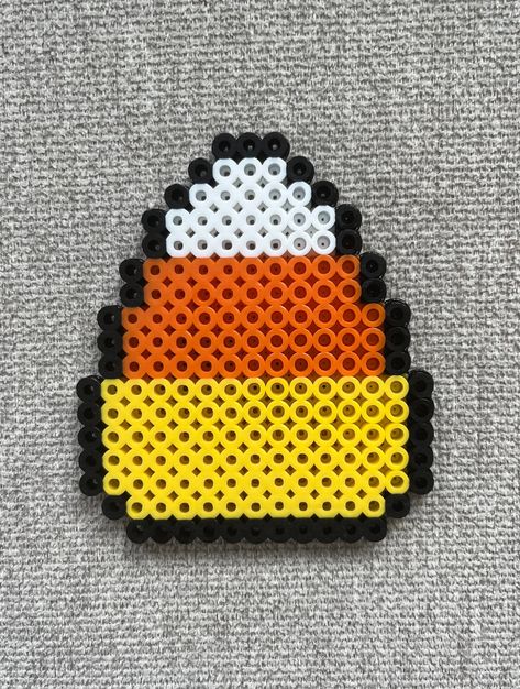 Candy corn perler bead magnet made with yellow, orange, white, and black beads. Cute Food Perler Beads, Perler Bead Magnet Patterns, Perler Bead Patterns With Clear Beads, Perler Bead Patterns Coraline, Perler Beads Black And White, Melting Beads Ideas Halloween, Peeler Beads Patterns Halloween, Melty Beads Ideas Easy Cute, Camping Perler Beads