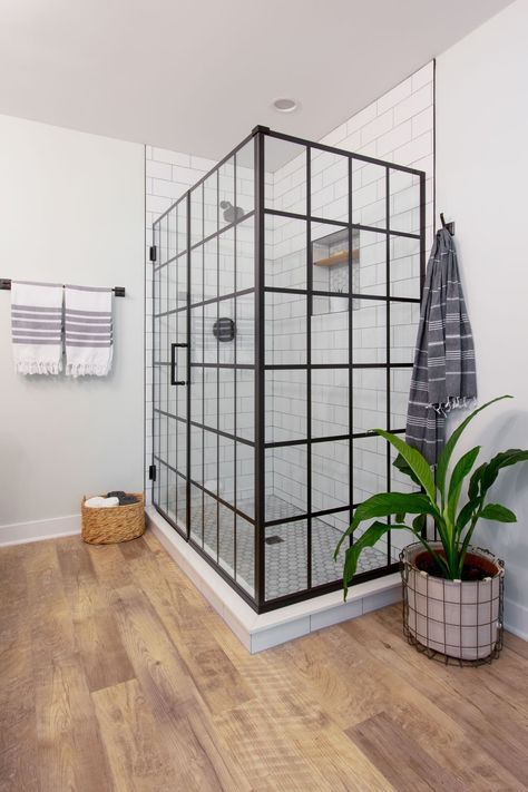 The Dreamline shower door adds a modern touch to the boho bathroom. The light, airy space features a large walk-in shower, black double vanity and hexagon accent tile. The space includes industrial touches, warm wood accents, and a vintage black and white color scheme. #bohobath #bohobathroom #bohochic Modern Boho Bathroom Floor Tile, Light And Airy Bathrooms, Bathroom Black Vanity Wood Floor, Black And White Bathroom With Wood Floor, Black And White Bathroom Wood Floor, Black White And Wood Bathroom, Dreamline Shower Door, Ultimate Bathroom, Dreamline Shower