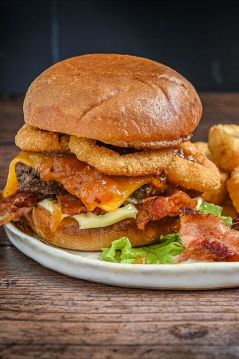 Our take on the classic BBQ Rodeo Cheeseburger. Think crispy onion rings, sweet and spicy BBQ sauce, bacon, and melted cheddar cheese on a juicy beef patty. Try it and you’ll be hooked! Rodeo Burger, Crispy Onion Rings, Spicy Bbq Sauce, Burger Recipes Beef, Parsley Salad, Bacon Tomato, Crispy Onions, Beef Patty, Beef Dishes