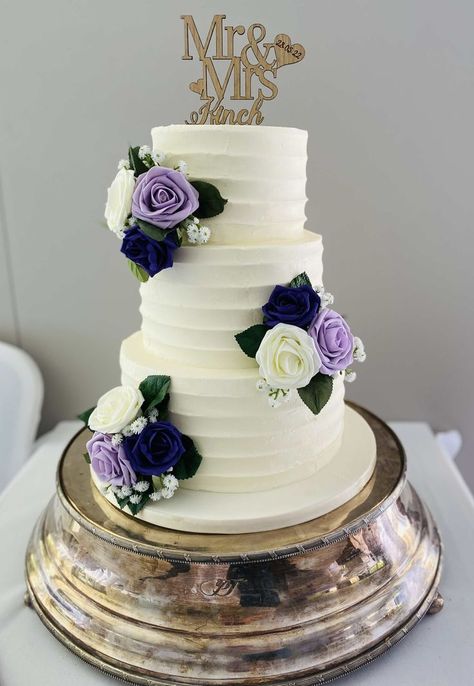 3 tier ridged buttercream wedding cake decorated with clusters of purple, lilac and cream foam roses & artificial leaves & gypsophilia and a personalised topper Navy Blue And Lavender Wedding Reception, Simple Wedding Cake With Purple Flowers, Navy Blue And Purple Wedding Cake, Purple Blue Wedding Cake, Wedding Cake Purple And Blue, Simple 3 Tier Wedding Cake, Wisteria Cake, Purple And Gold Wedding Cake, Lilac Wedding Cake