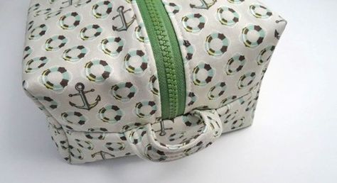 9: Separate the two layers of outer fabric. Pin a handle to each end of the Dopp kit around the zipper as shown in the photo below. 10: Make sure all layers (lining and outer) are aligned well, pin. Stitch each aligned short end of the Dopp kit with a 3/8″ seam. Stitch slowly over the zipper to avoid breaking your needle. Trim any excess zipper tape if desired. Finish seam allowances if desired. 11: Turn the Dopp kit right side out through one of the rectangular corner cuts. It may seem sl Dopp Kit Tutorial, Toiletry Bag Pattern, Tote Tutorial, Dopp Bag, Diy Sewing Gifts, Diy Bag Designs, Pouch Tutorial, Simple Sewing, Box Pouch