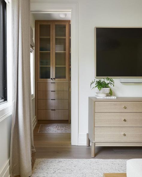 A light brown wooden dresser with brass knobs is placed beneath a large wall mounted TV. Tv Above Dresser, Mirror Dresser Decor, Wall Mounted Tv Bedroom, Tv In Bedroom Ideas, White Dresser Decor, Living Room Design Black, Built In Bedroom Cabinets, Above Dresser, Bedroom Dresser Styling