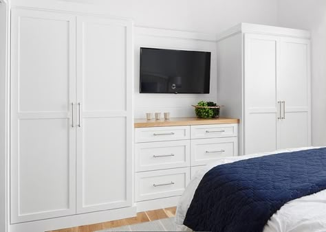 White built-in wardrobes flank a built-in dresser accented with a wood top and fixed beneath at flat panel television. Built In Dresser In Bedroom Chest Of Drawers Closet Ideas, Bedroom Storage With Tv, Bedrooms With Built In Storage, Built In Closet Tv Bedroom, Built In White Wardrobes, Wardrobe Master Bedrooms Built Ins, Where To Put Wardrobes In Bedroom, Bedroom Built Ins With Tv, Built In Wardrobe With Dresser