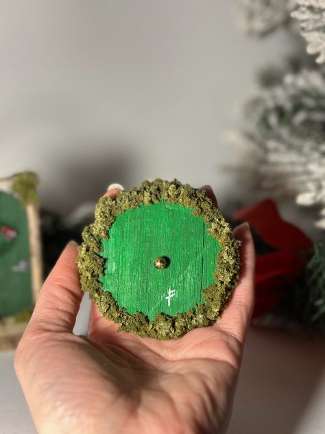 These unique mini Hobbit doors are carved and hand-painted, decorated around a grapevine wreath with moss, faux foliage, and an antique (color) brass knob. Perfect as a Christmas tree ornament or even a subtle decoration to your living room, office, or bedroom! This art piece is delicate and fragile and to be handled with care. Lord Of The Rings Christmas, Hobbit Decor, Hobbit Doors, Lord Of The Rings Gift, Hobbit Door, Door Ornament, Brass Knob, Brass Knobs, Handmade Ornaments