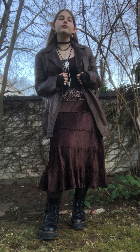 A mid-size person/girl wearing mate rose lipstik, a black tight waistcoat with a ripped stocking selfmade longsleeve and a thrifted dark brown maxi skirt, black dr. Martins and multiple crystal rings and bracelets. 	The person is also wearing multiple silver necklaces, one in form of a dragonfly and another in form of a moon, a green crystal bead necklace and a black lace choker. Grunge Trench Coat Outfit, Fairy Punk Outfits, Fairy Grunge Costume, Earth Witch Aesthetic Outfit, Dark Naturalism Outfits Aesthetic, Dark Cottage Core Fashion, Dark Cottagecore Aesthetic Outfits, Dark Cottage Core Outfits, Forest Core Outfits