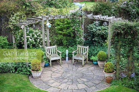 View of circular seating area and pergola in private garden. Circular Patio Ideas Landscaping, Circle Patio Ideas Landscape Design, Seating Area In Middle Of Garden, Cottage Garden Seating Area, End Of Garden Seating Area, Round Seating Area Garden, Circular Patio Design, Circular Pergola, Round Patio With Pergola