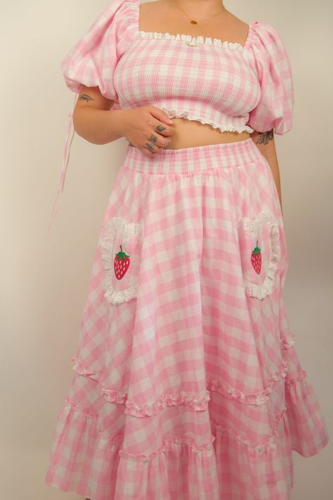 Our pastel pink gingham Strawberry Blossom Top is back! This cotton top flaunts a center rosette detail, billowy sleeves with delicate ribbons to tie, along with front and back shirring for an impeccable fit. Complete the look with our matching Strawberry Blossom Skirt or mix it up with jeans. Ideal for an outdoor concert, bring a friend along for the adventure! Details: Cotton Rosette detail Ribbon ties Front and back shirring Model is wearing size Medium. Cute Apple Shape Outfits, Kawaii Clothing Aesthetic, Cute Strawberry Dress, Strawberry Shortcake Fashion, Cute Pink Winter Outfits, Cute Spring Tops, Kawaii Wardrobe, Strawberry Fashion, Embroidered Strawberries