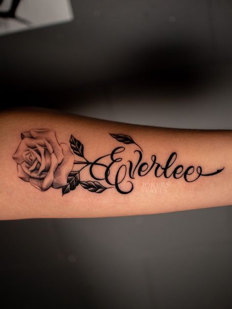 Flower Arm Tattoo With Name, Flower With Name Tattoo Ideas, Roses And Name Tattoo, Rose Tattoos With Names Stem, Name Tattoos With Rose, Name Tattoo Forearm Woman, Spouses Name Tattoo Ideas, Tattoo Ideas Of Names, Rose And Name Tattoo Design