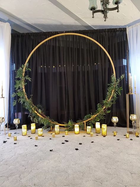 Gold Circle Arch, greenery and black draping. Message today for a free quote Circle Photo Backdrop, Black And Gold Wedding Backdrop, Gold Hoop Backdrop, Circle Arch Wedding Backdrop With Lights, Black And Gold Backdrop Ideas, Circle Wedding Arch Greenery, Greenery Circle Arch, Gold Circle Backdrop, Gold Circle Arch With Greenery