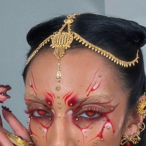 ROWI SINGH⚡️🌻 on Instagram: "Forgot to post the photos from this look 👹 combining culture and editorial makeup 🤝🏽✨  Earrings: @bunx.store // @theofficialpandora  Cuffs and necklaces @the.olio.stories   Using @glisten_cosmetics red wet liner and spectra mascara in orange red  @anastasiabeverlyhills medium contour kit @embellishbyrowi mercurial studs @beautybaycom brights 2.0 palette  @makeupforever limitless brown lip liner + @halfmagicbeauty mouth cloud + @fentybeauty hot chocolit glossbomb heat   #editorialmakeup #graphicliner" Red Makeup Creative, Wet Makeup Look Editorial, Red Graphic Liner Makeup, Rowi Singh Makeup, Red Liner Makeup, Red Editorial Makeup, Red Face Makeup, Olio Stories, Red Halloween Makeup