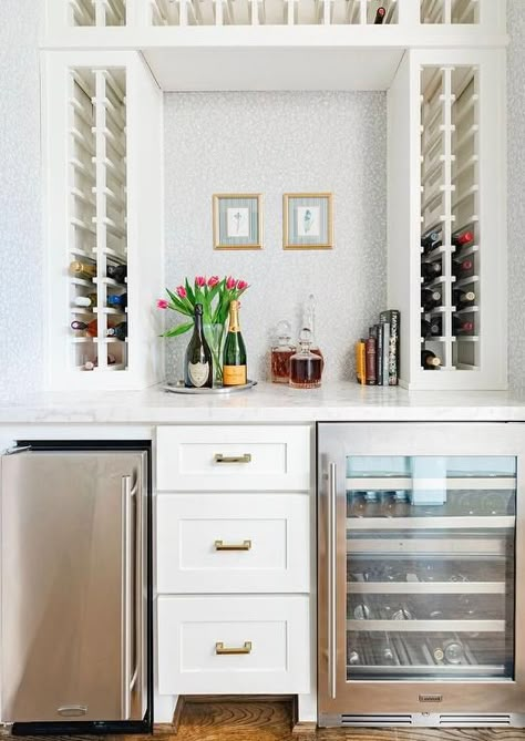 Built-in wine racks frame a white and gray wallpapered wall holding gold framed art over white drawers flanked by a stainless steel beverage fridge and a glass-front wine fridge. Built In Bar Cabinet, Wet Bar Cabinets, Gold Framed Art, Fridge Design, Built In Wine Rack, Outdoor Kitchen Cabinets, Beverage Fridge, Interiors Photography, Kitchen Finishes