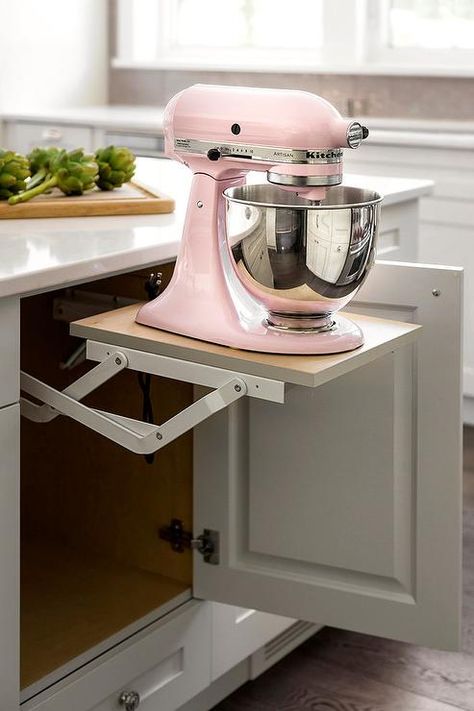 A pink KItchenAid Mixer sits atop a pop up shelf fixed beneath a white island finished with white cabinets adorned with polished nickel knobs. Pink Kitchenaid, Pink Kitchenaid Mixer, White Island, Outdoor Kitchen Appliances, Kitchenaid Mixer, Kitchen Island Decor, Modern Kitchen Island, Diy Kitchen Island, Island Decor