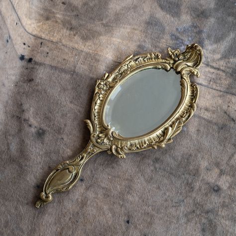 Antique hand held mirror Gold tone hand mirror Style: Victorian Old ornate vanity mirror made of heavy solid brass Measurements:  4" x 10" (10,5 cm x 26 cm) Good vintage condition. Old piece shows charming signs of age and wear, patina (see photos and video) 👉 More vintage vanity mirrors from my shop http://etsy.me/2NKiLui Cintage Mirror, Antique Hand Held Mirror, Ancient Mirror Aesthetic, Aesthetic Hand Mirror, Mirror Still Life, Antique Handheld Mirror, Vintage Mirror Aesthetic, Old Hand Mirror, Antique Shop Aesthetic