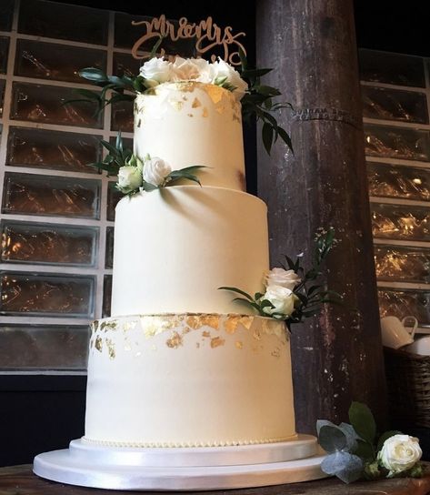 This ivory wedding cake was decorated with a smooth buttercream finish, edible gold leaf and fresh flowers. 3 tiers of luscious lemon cake and held at the trendy modern venue clapton country club in Hackney, East London. #eastlondonwedding #eastlondon #londonwedding #trendywedding #buttercream #buttercreamcake #buttercreamweddingcake #goldleaf #edibleart #ediblegoldleaf #stylishweddingcake #modernweddingcake #showstoppercake #showstopperweddingcake #beautifulweddingcake #simpleweddingcakes Wedding Cake With Gold Flakes, Gold Leaf Wedding Cake, Wedding Cake Gold Leaf, Buttercream Ruffles, Smooth Buttercream, Showstopper Cakes, Ivory Wedding Cake, Ruffle Wedding Cake, Edible Gold Leaf