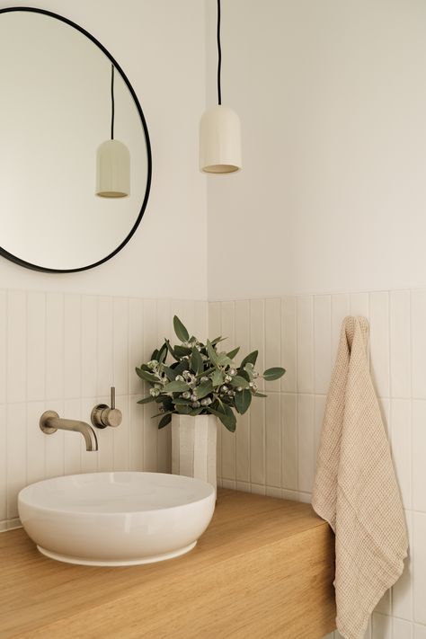 Corner view of a timber bathroom vanity, white vertical tiled splashback and black framed round mirror sitting above a white round sink Nordic Powder Room, Small Splashback Bathroom, Powder Room Splashback, Powder Room White Tile, Bathroom Ideas Scandinavian Style, Vanity Splashback Tiles, Tile Splashback Bathroom Sink, White Vertical Tiles Bathroom, Modern Scandi Bathroom