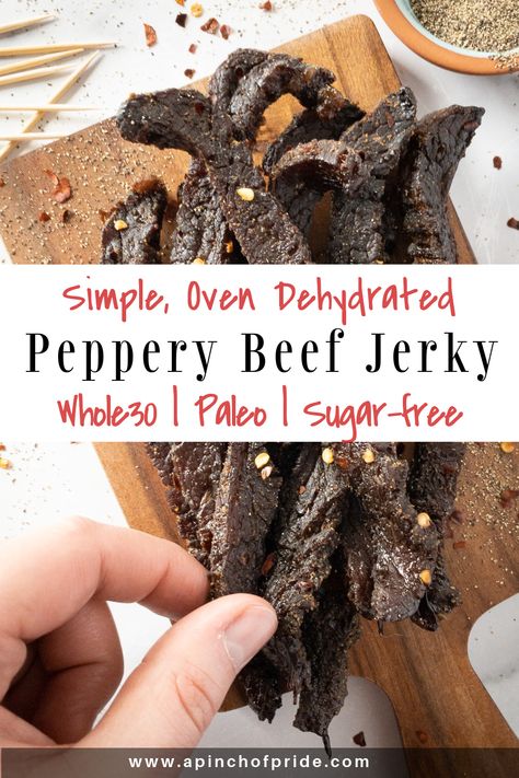 Hand grabbing a slice of peppery beef jerky. Jerky is on a wooden board sprinkled with red pepper flakes and ground pepper. There are a few toothpicks on the top left. Tag says "Simple, Oven Dehydrated Peppery Beef Jerky. Whole30, paleo and sugar-free." Beef Jerky Recipe Dehydrator, Beef Jerky Marinade, Jerky Recipes Dehydrator, Oven Jerky, Jerky Marinade, Making Beef Jerky, Smoked Beef Jerky, Best Beef Jerky, Jerky Recipe