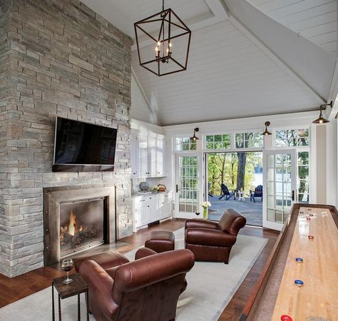 Chic, long game room features a vaulted paneled ceiling over a floor to ceiling gray stone fireplace lined with a tilted flat panel TV over a metal fireplace placed before a pair of brown leather recliners and an extra long shuffleboard table. Darlana Lantern, Grey Stone Fireplace, Cottage Mansion, Shingle Style Architecture, Restoration Hardware Style, Lake House Interior, Lake Houses Exterior, Lake Minnetonka, Shuffleboard Table