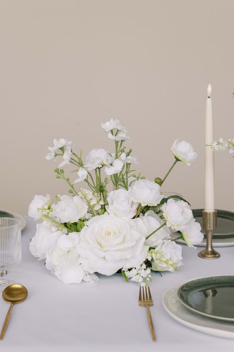 The Audrey vaseless centerpiece is made of mixed ivory and white silk flowers. It features Diana roses  rose buds  french rose spray  camellia spray  and hydrangeas. It is accented with larkspur spray and lily of the valley for added texture. This vaseless centerpiece design can be used in a variety of ways and matches any decor aesthetic. Premium silk florals.The Audrey vaseless centerpiece measures 11 tall by 10” wide and is part of the Audrey Collection., Lily Flowers Wedding Decor, Cotton Centerpiece Table Decorations, Flowers And Candles, Low White Flower Centerpieces, Low White Rose Centerpiece, White Floral Runner Centerpiece, White Floral Compote Centerpiece, Elevated Floral Centerpieces White, Cocktail Table Centerpieces