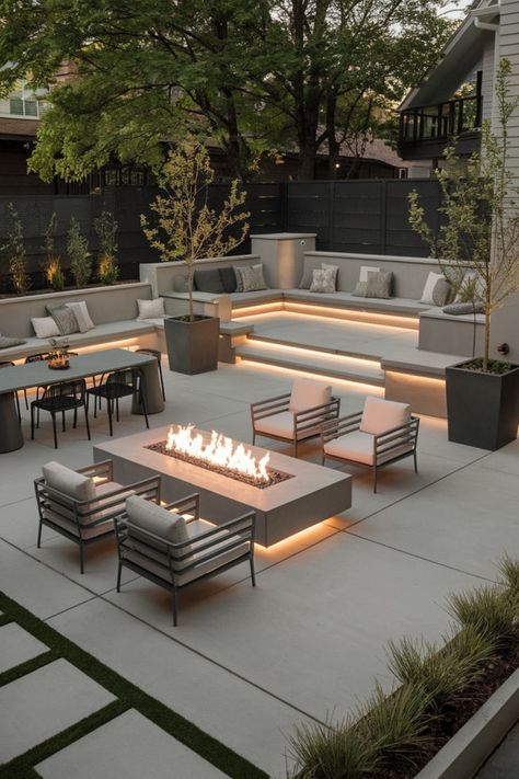 Upgrade your outdoor space with this luxurious modern patio. Highlighted by a smooth concrete fire pit and built-in stone seating, the area also features sleek lounge furniture and a relaxing ambiance. Surrounded by lush greenery and illuminated with subtle lighting, this design is the ultimate backyard retreat. #ModernPatioIdeas #BackyardLuxury #FirePitDesign #OutdoorLivingSpace #StoneSeating #GreeneryDecor Modern Outdoor Fireplace Patio, Paver Backyard Ideas Landscapes, Backyard Modern Ideas, Contemporary Outdoor Spaces, Exterior Lounge Design, Contemporary Backyard Landscaping Ideas, Concrete Garden Seating, Stone Outdoor Furniture, Outdoor Fire Feature