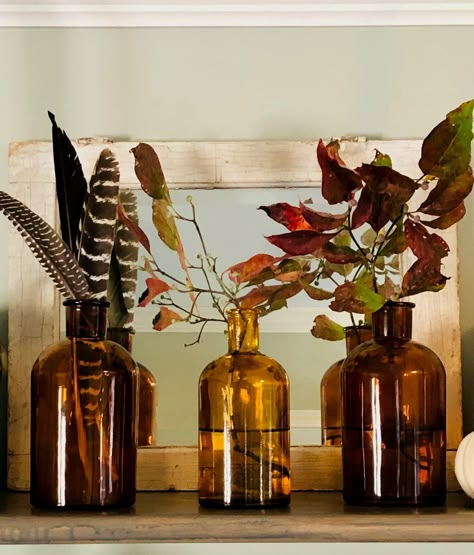 Amber bottles are a super inexpensive way to add warmth to your decor. Amber Jug Centerpiece, Fall Amber Glass Decor, Brown Bottle Centerpiece, Amber Decor Inspiration, Brown Glass Bottles Decor, Amber Vase Decor, Amber Home Decor, Amber Glass Christmas Decor, Brown Bottle Decor