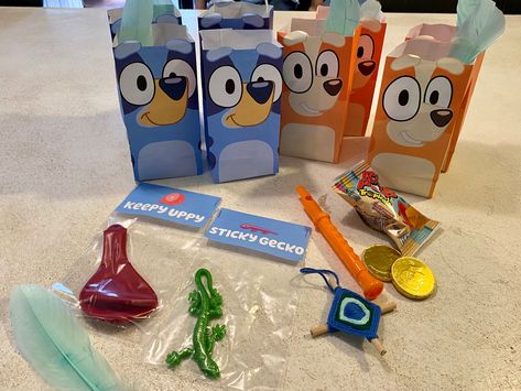 Bluey treat bags made from printable on the Bluey website. Included: stucky gecko, a balloon for keepy uppy, a featherwand, a mini God’s eye, two gold coins (two dollarbucks), a whistle, and candy! Not pictured: inflatable guitars! #Bluey #Blueybirthday #Blueybirthdayparty #Kidsbirthday #party #partybackdrop #diy #diybirthday #treat #treatbag Bluey Birthday Candy Bags, Diy Bluey Goodie Bag, Bluey Birthday Treat Bags, Diy Bluey Gift Bags, Bluey Party Bag Ideas, Bluey Birthday Party Goody Bags, Bluey Birthday Party Gift Bags, Bluey Birthday Gift Bags, Bluey Goodie Bags Favors