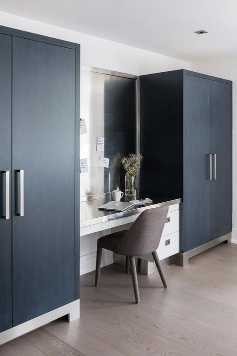 A magnetic board is hung between tall black cabinets and over a white built-in desk finished with a stainless steel desktop. Sherwin Williams Magnetic Gray, White Upper Cabinets Dark Lower, Oval Kitchen Island, Dark Lower Cabinets, Den Library, White Upper Cabinets, Brown Cowhide Rug, Desk Nook, Top Kitchen Cabinets