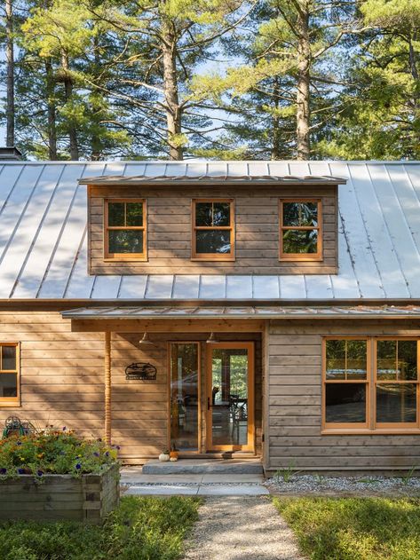 Cedar wood exterior siding with a brown stain keeps this Maine summer camp camouflaged in its surroundings. Orange hemlock posts and trim provide a contemporary chic touch while maintaining the rustic inspiration. Cedar Contemporary House, Contemporary Rustic Exterior, Cedar Shake Cabin, White And Cedar Exterior, Maine Modern Cabin, Brown Cedar House Exterior, Horizontal Wood Siding Exterior, Lake Cabin Exterior Colors, Cabin In The Woods Exterior