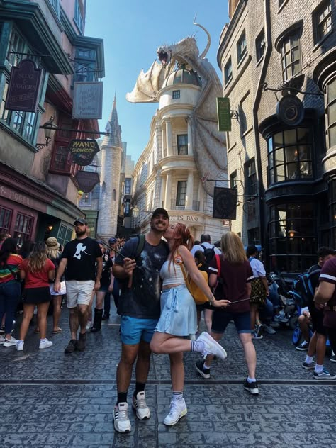 Photo of couple in front of gringotts bank at diagon alley in the wizarding world of harry potter at universal studios orlando. Both people hold a harry potter wand, girl is kissing boy on the cheek with a foot popped. Universal Studios Orlando Couple Photos, Couple Universal Studios, Universal Studios Couple Outfit, Universal Studios Outfit Couples, Universal Studios Photo Ideas Couple, Universal Couple Pictures, Universal Studios Couple Pictures, Harry Potter World Outfit Summer, Universal Studios Instagram Pictures