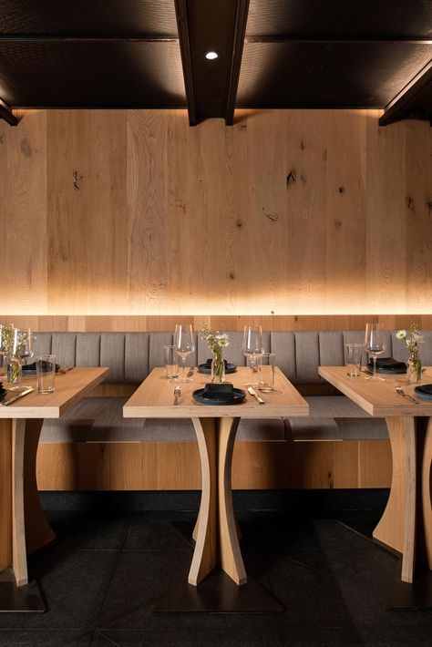 This modern restaurant has a high vaulted ceiling, wood walls, hidden lighting, an expansive bar, and various dining areas, including booth and banquette seating. #RestaurantInterior #ModernRestaurant #BarInterior #BarDesign