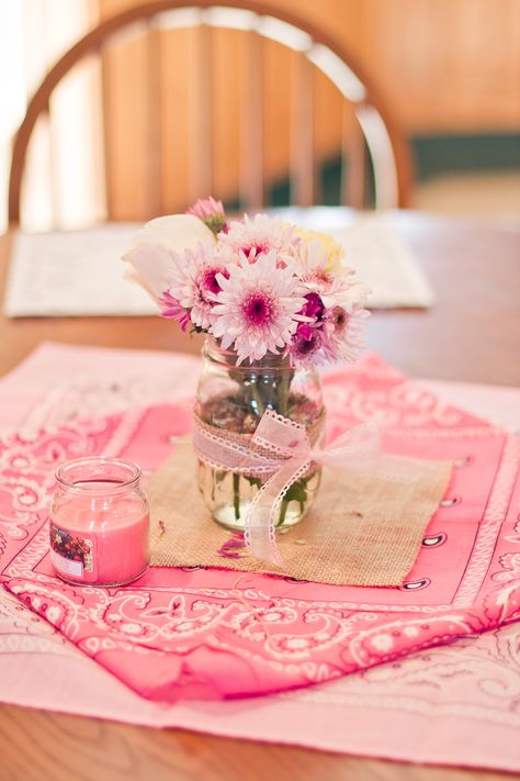 Simple pink bandanas (Michaels) with a piece of burlap on it (Amazon), a mason jar wrapped with a strip of burlap and ribbon, and some assorted flowers. These were the table centerpieces. #vintagecowgirl #cowgirlparty Pink Cowgirl Party Centerpiece, 1st Rodeo Centerpieces Pink, Cowgirl Themed Centerpieces, Rodeo Birthday Party Centerpieces, Pink Western Centerpiece Ideas, Bandana Centerpiece Ideas, Pink Country Birthday Party, Cowgirl Table Centerpieces, Pink Farm Centerpiece