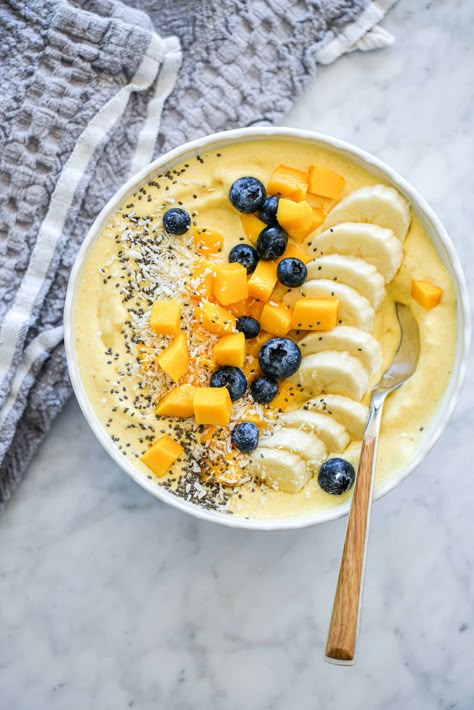 Mango smoothie with wooden and silver spoon in a bowl topped with sliced banana, chopped mango, blueberries, chia seeds, and coconut flakes Easy Mango Smoothie, Smoothie Bowls Aesthetic, Mango Aesthetic, Mango Drink, Rainbow Recipes, Mango Smoothie Bowl, Mango Banana Smoothie, Sliced Banana, Yoghurt Bowl