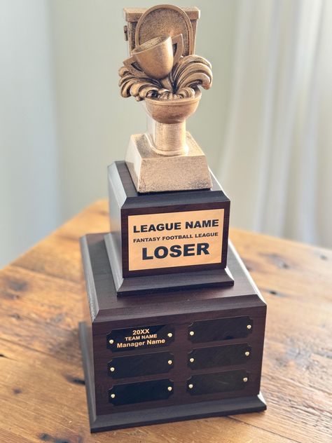 Elevate your fantasy football league with this prestigious perpetual trophy. Crafted for enduring legacy that honors the loser of your league. This magnificent piece features a toilet that is meant to "honor" the loser of your league. The resin figure is mounted on a cherry finish base. Year after year, celebrate your league's loser by adding a personalized nameplate to the trophy's base. The base comes with six plaques and can fit up to 24 perpetual plaques for up to 24 years of winners.  FREE Trophy Base, The Loser, Fantasy Football League, Awards Trophy, Fantasy Football, Team Names, Name Plate, Qr Code, Photo Gallery