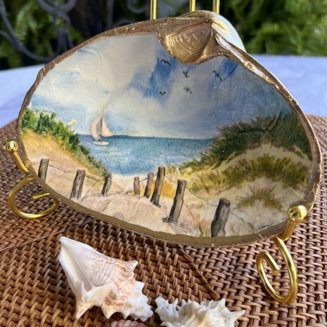 This Large Clamshell is adorned with a peaceful, tranquil seashore scene. Uniquely handcrafted, this beautiful piece effortlessly combines art and functionality to bring a touch of elegance to your home. The soft color palette, predominantly in serene blues and greens, further enhances the peaceful ambiance. Gilding has been applied to the back and edges to bring a touch of opulence, enhancing the already enchanting design.  Each shell measures approximately 7" across and 4.5" from the top of th Clamshell Crafts, Seashell Decoration, Painting Seashells, Decoupage Shells, Painted Seashells, Sand Dollar Ornament, Memory Ring, Shell Painting, Seashell Projects