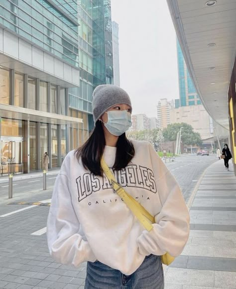 girl standing maybe in seoul korea wearing a beanie and face mask. has her hands in her jean pockets and is wearing a white los angeles over sized sweather with yellow crossbody bag Outfit Inspo Asian, Street Style Seoul, Chinese Street Style, Korean Style Outfit, Fashion Beanie, Girl Streetwear, Seoul Fashion, Fashion Korean, Double Tap