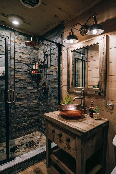 A rustic tiny house bathroom featuring a stone-tiled shower, a wooden vanity with a copper basin sink, and a mirror framed with repurposed barn wood. Log House Bathroom, Rustic Tiny House Interior, Cabin Style Bathroom, Tiny House Interior Design Ideas, Farmhouse Bathroom Inspiration, Industrial Farmhouse Bathroom, Rustic Tiny House, House Interior Design Ideas, Farmhouse Bathroom Ideas