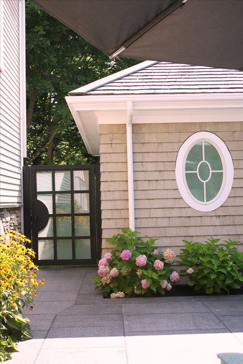 An oval window and a custom glass and iron garden gate bring style and privacy to this pool area. Exterior Oval Window, Small Round Window Ideas, Oval Windows Ideas, Oval Windows Exterior, Den Bookshelves, Attic Ceiling, Oval Windows, Round Windows, Nantucket Style Homes