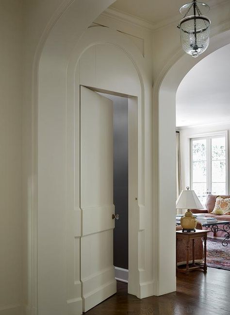 An off-white hidden powder room door is positioned beside an arched doorway and illuminated by a Greek key glass lantern. Hidden Powder Room Door, Hidden Powder Room, Arched Doors Interior, Spanish Style Home Interior, Speakeasy Decor, Arch Doorway, Lexington Home, Entrance Foyer, Hidden Rooms