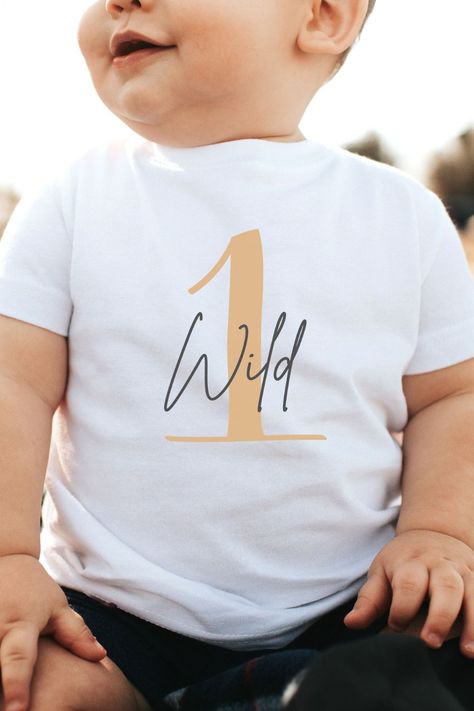 baby in a white shirt with a tan one on it and wild handwritten on the front of it 1st Birthday Shirts Boy, One Year Old T Shirt Ideas, One Year Old Birthday Shirt, Wild One Party Shirts, Wild One T Shirt, Cute White T-shirt For First Birthday, First Birthday Boy Outfit, The Wild One First Birthday Boy Shirt, Wild One Birthday Shirt